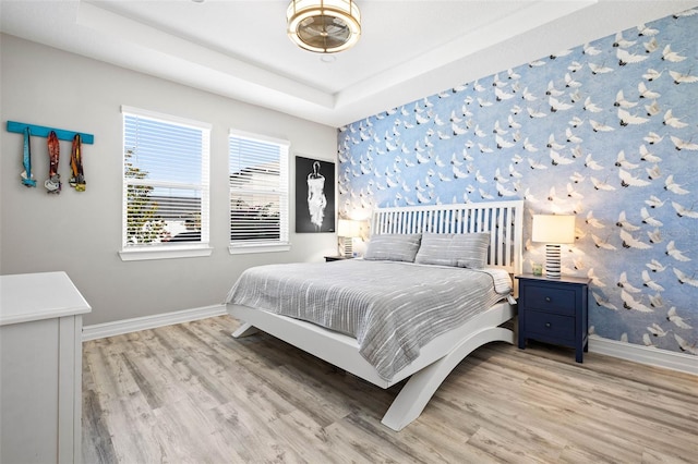 bedroom featuring baseboards, light wood-type flooring, and a tray ceiling