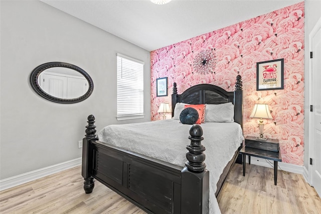 bedroom featuring baseboards, wood finished floors, and an accent wall