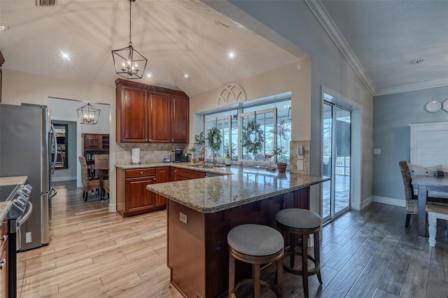 kitchen with a chandelier, light wood finished floors, a peninsula, a breakfast bar area, and ornamental molding