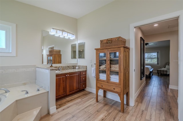 ensuite bathroom with wood finished floors, a bath, vanity, baseboards, and ceiling fan