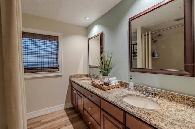 full bath with wood finished floors, baseboards, double vanity, and a shower