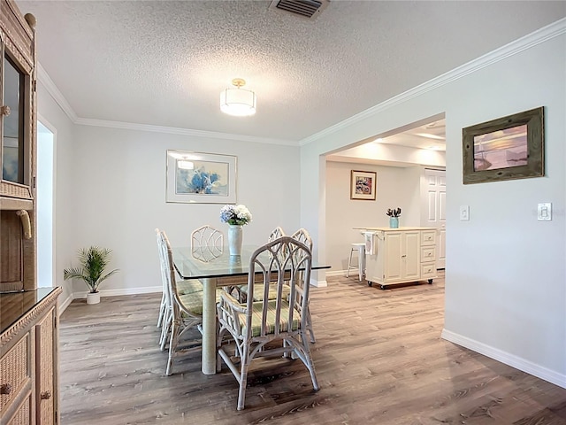dining room featuring light wood-style flooring, crown molding, baseboards, and a textured ceiling