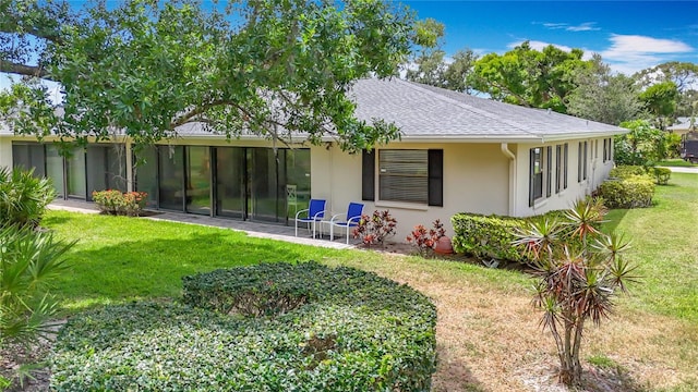 rear view of property featuring stucco siding, a lawn, and roof with shingles