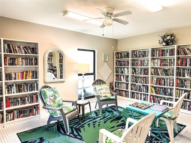 living area with wall of books, ceiling fan, and tile patterned floors
