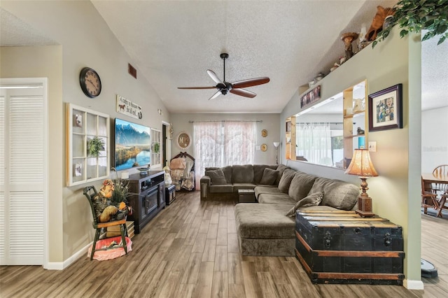 living room featuring wood finished floors, a ceiling fan, a textured ceiling, lofted ceiling, and baseboards