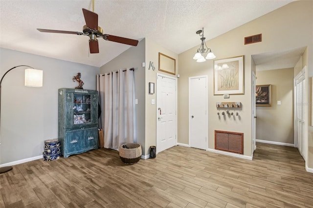 foyer entrance with vaulted ceiling, wood finished floors, baseboards, a ceiling fan, and a textured ceiling
