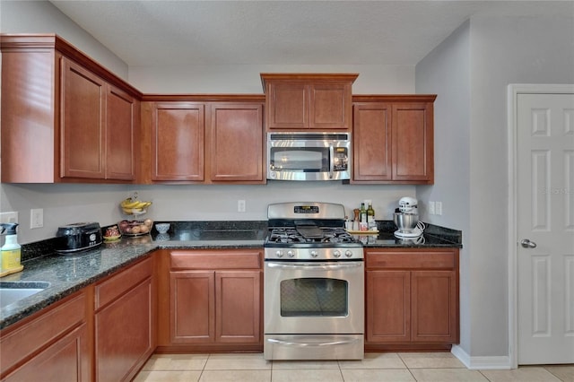 5914 Goldenbark Pl, Lithia, FL 33547 - kitchen featuring stainless steel appliances, dark stone countertops, light tile patterned floors, and brown cabinets