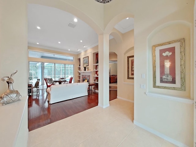 16343 Burniston Dr, Tampa, FL 33647 - living room with crown molding, a warm lit fireplace, arched walkways, baseboards, and light tile patterned flooring