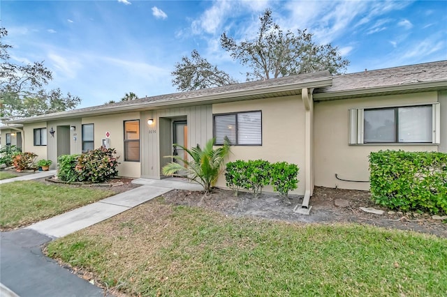 single story home featuring a front lawn, stucco siding, and roof with shingles