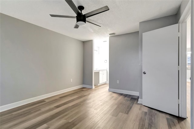 unfurnished bedroom featuring wood finished floors, baseboards, a textured ceiling, ensuite bathroom, and ceiling fan