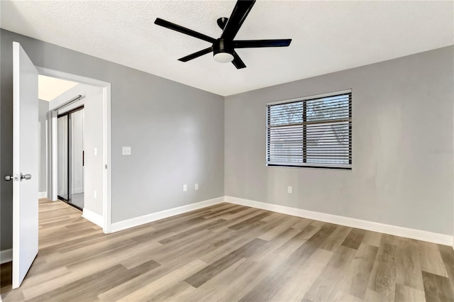 empty room featuring ceiling fan, light wood-style flooring, baseboards, and a textured ceiling