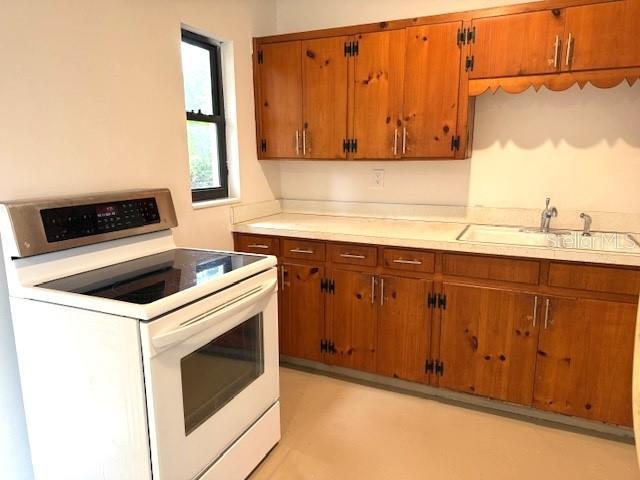 1138 Huss Rd, Wauchula, FL 33873 - kitchen featuring white range with electric stovetop, brown cabinets, light countertops, and a sink
