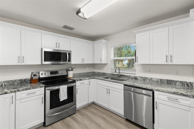 3119 W N St, Tampa, FL 33614 - kitchen with stainless steel appliances, a sink, light wood-style flooring, white cabinets, and dark stone countertops