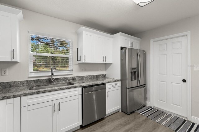 3119 W N St, Tampa, FL 33614 - kitchen featuring stainless steel appliances, a sink, light wood finished floors, white cabinets, and dark stone countertops