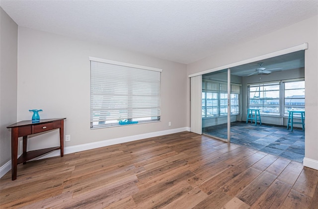 empty room with hardwood / wood-style flooring, a ceiling fan, baseboards, and a textured ceiling