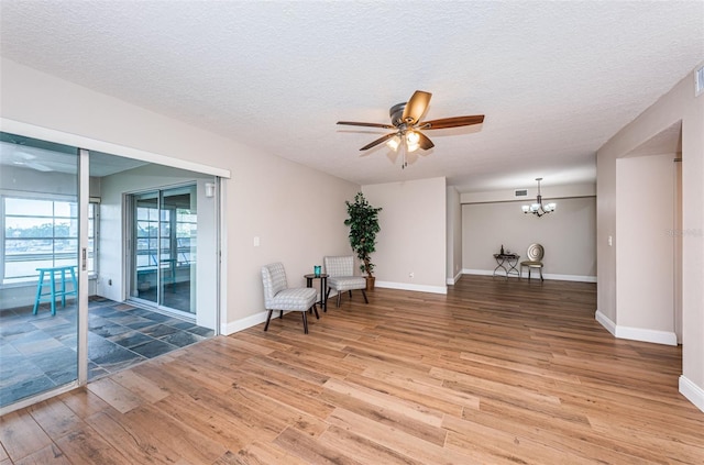 living area featuring a ceiling fan, light wood-style floors, a textured ceiling, a chandelier, and baseboards