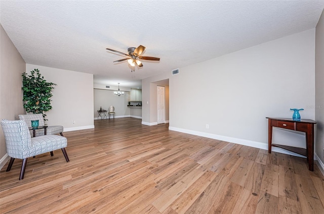 unfurnished room with ceiling fan, light wood-style flooring, a chandelier, baseboards, and a textured ceiling