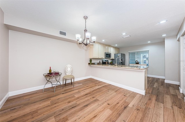 kitchen with appliances with stainless steel finishes, a peninsula, light wood-type flooring, recessed lighting, and baseboards