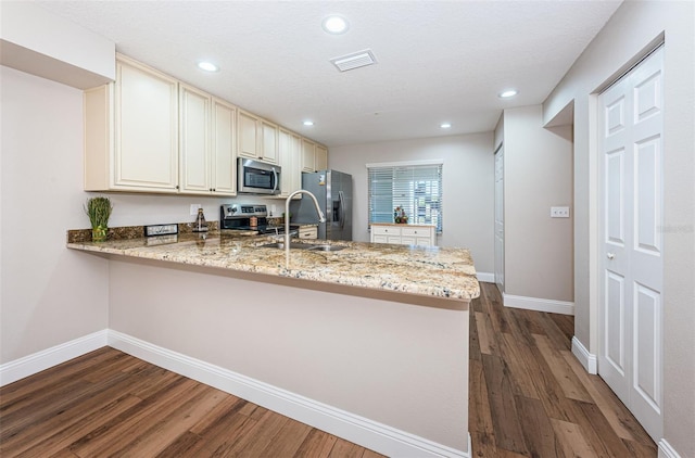 kitchen featuring stainless steel appliances, a peninsula, dark wood-style flooring, a sink, and cream cabinetry