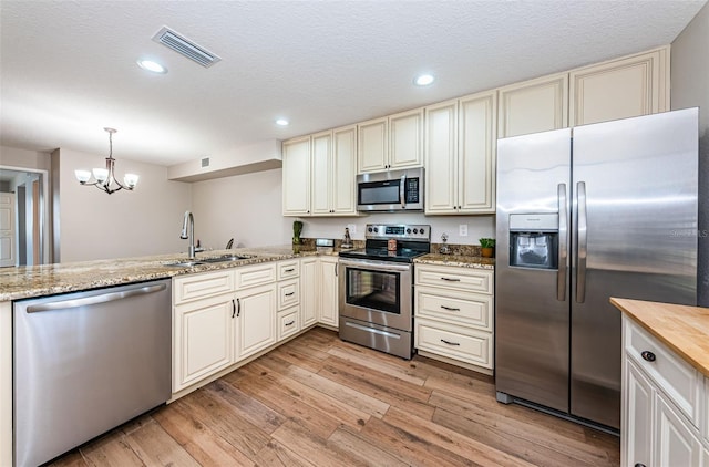 kitchen featuring appliances with stainless steel finishes, a sink, a chandelier, cream cabinetry, and light wood finished floors