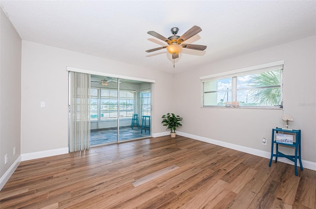 empty room with a ceiling fan, wood finished floors, and healthy amount of natural light