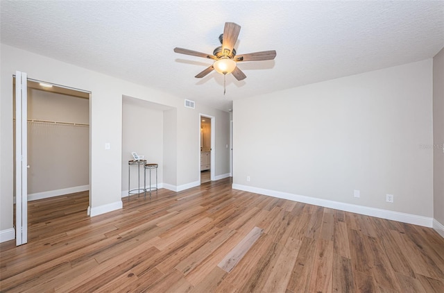 unfurnished bedroom with light wood finished floors, a closet, baseboards, a walk in closet, and a textured ceiling