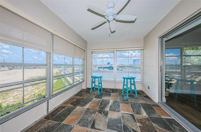 sunroom / solarium with stone tile flooring, a ceiling fan, and healthy amount of natural light