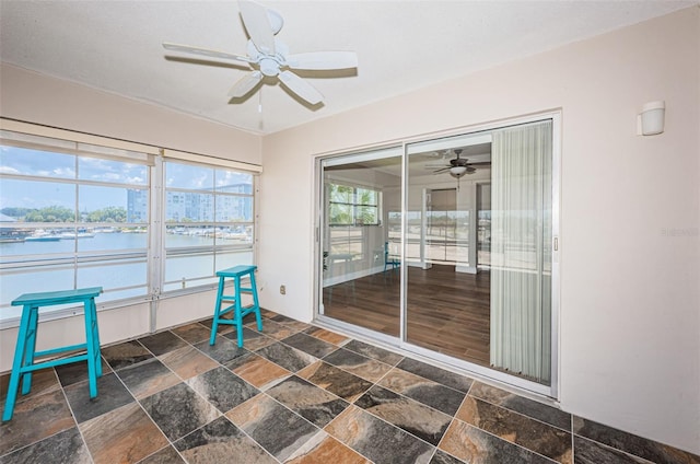 unfurnished sunroom with ceiling fan and a water view