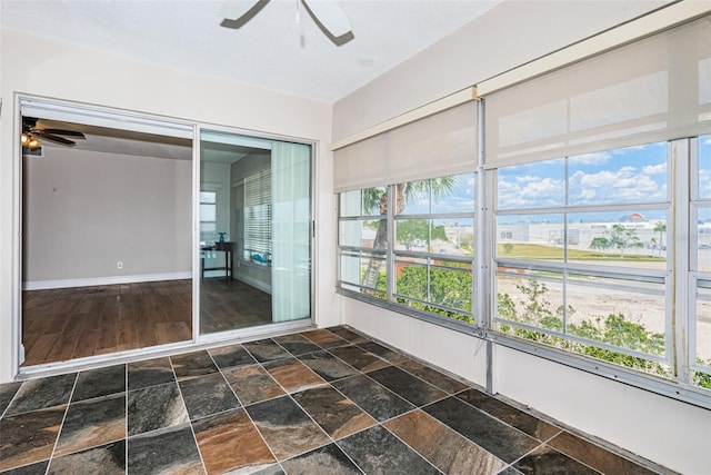 unfurnished sunroom featuring a ceiling fan, stone finish flooring, and baseboards