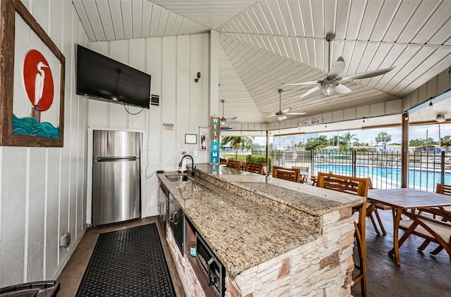 view of patio / terrace featuring fence, a ceiling fan, exterior kitchen, and a bar