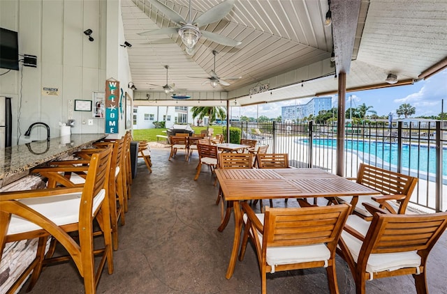 view of patio with outdoor dining area, fence, a community pool, and ceiling fan