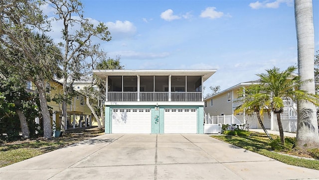 raised beach house featuring a sunroom, concrete driveway, an attached garage, and fence