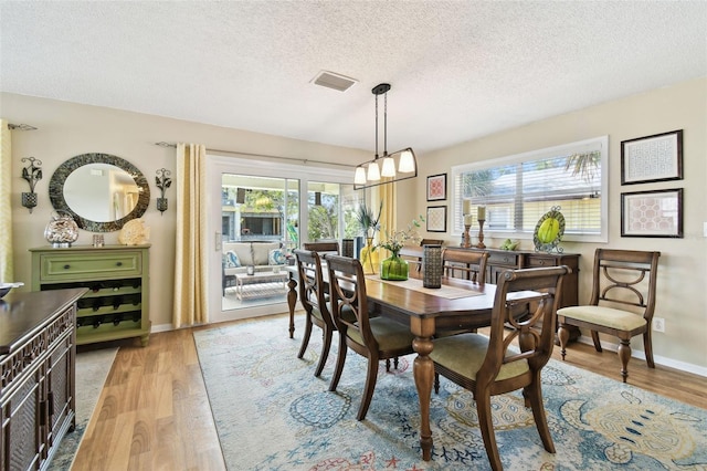 dining space with plenty of natural light, a textured ceiling, light wood-type flooring, and baseboards