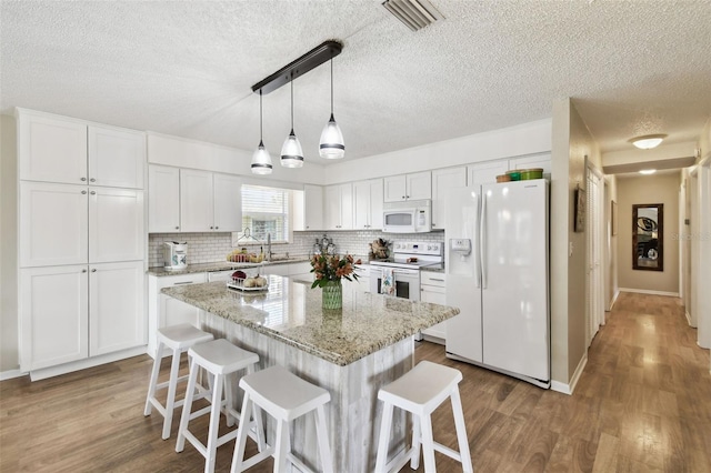 kitchen featuring white appliances, a textured ceiling, white cabinetry, and wood finished floors