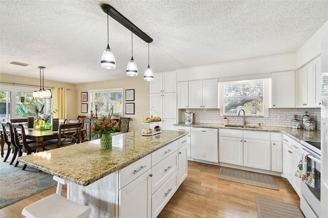 kitchen featuring white appliances, a sink, a textured ceiling, light wood finished floors, and backsplash