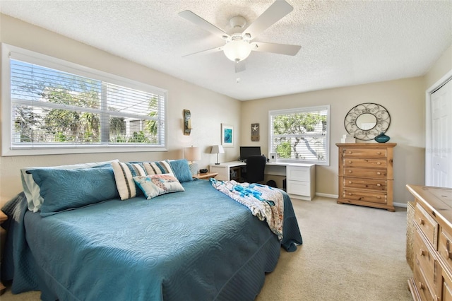 bedroom with light carpet, a textured ceiling, an office area, a ceiling fan, and baseboards
