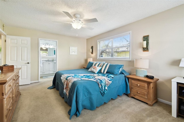 bedroom with light colored carpet, ensuite bathroom, a textured ceiling, a ceiling fan, and baseboards