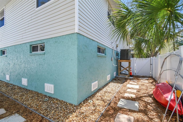 view of property exterior featuring a gate, stucco siding, fence, crawl space, and cooling unit