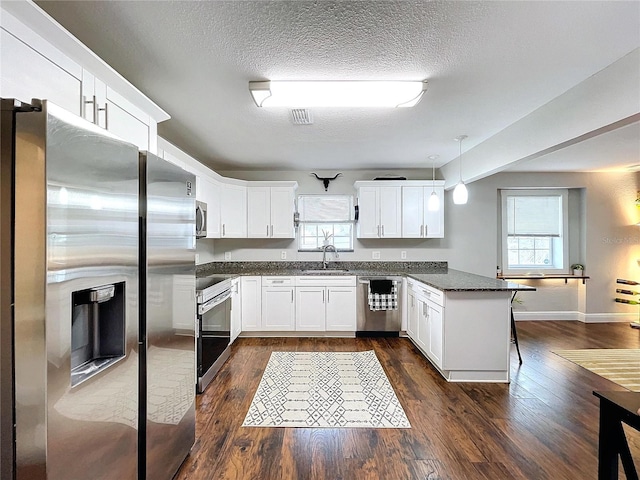 3213 E Genesee St, Tampa, FL 33610 - kitchen featuring appliances with stainless steel finishes, a sink, a peninsula, dark wood-style flooring, and white cabinets