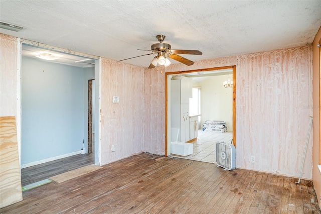 unfurnished room with hardwood / wood-style floors, ceiling fan, wooden walls, and a textured ceiling