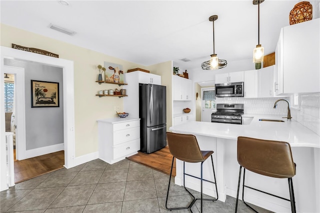 kitchen featuring stainless steel appliances, a sink, a peninsula, open shelves, and light countertops