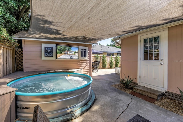 view of patio with an outdoor hot tub and fence