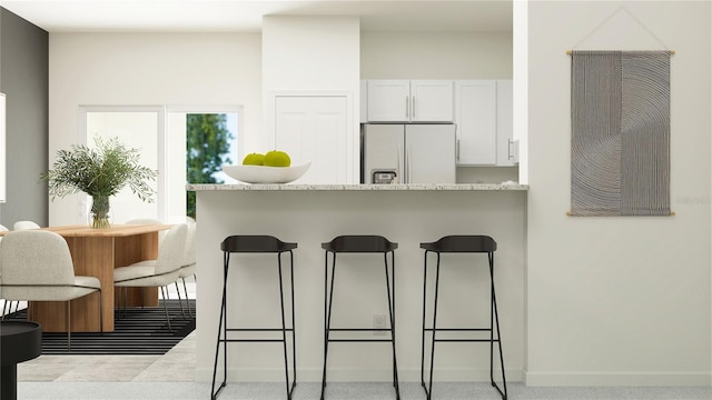 kitchen with white fridge with ice dispenser, a breakfast bar area, white cabinetry, baseboards, and light stone countertops
