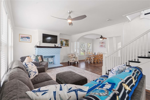 living room with a ceiling fan, wood finished floors, arched walkways, stairs, and ornamental molding