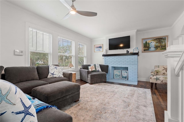 living area with ornamental molding, ceiling fan, a brick fireplace, wood finished floors, and baseboards