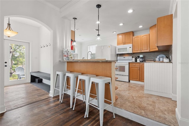 kitchen featuring white appliances, a kitchen bar, crown molding, a peninsula, and decorative backsplash