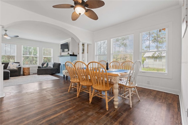 dining area with a ceiling fan, dark wood-type flooring, baseboards, crown molding, and arched walkways