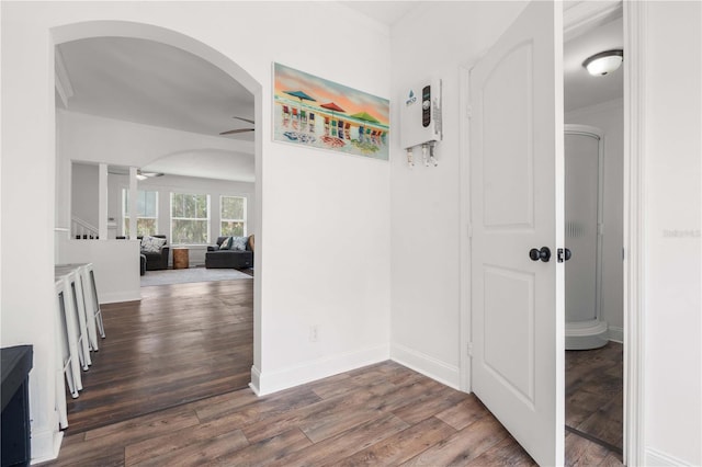 hallway with wood finished floors, arched walkways, baseboards, and ornamental molding