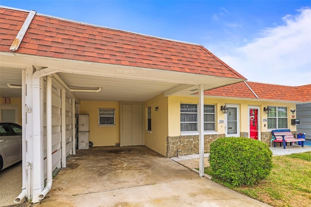 view of front of house featuring an attached carport, roof with shingles, and stone siding