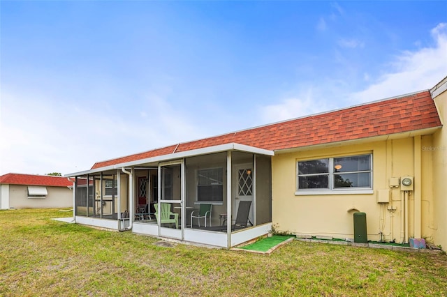 back of property featuring a sunroom, roof with shingles, a yard, and stucco siding